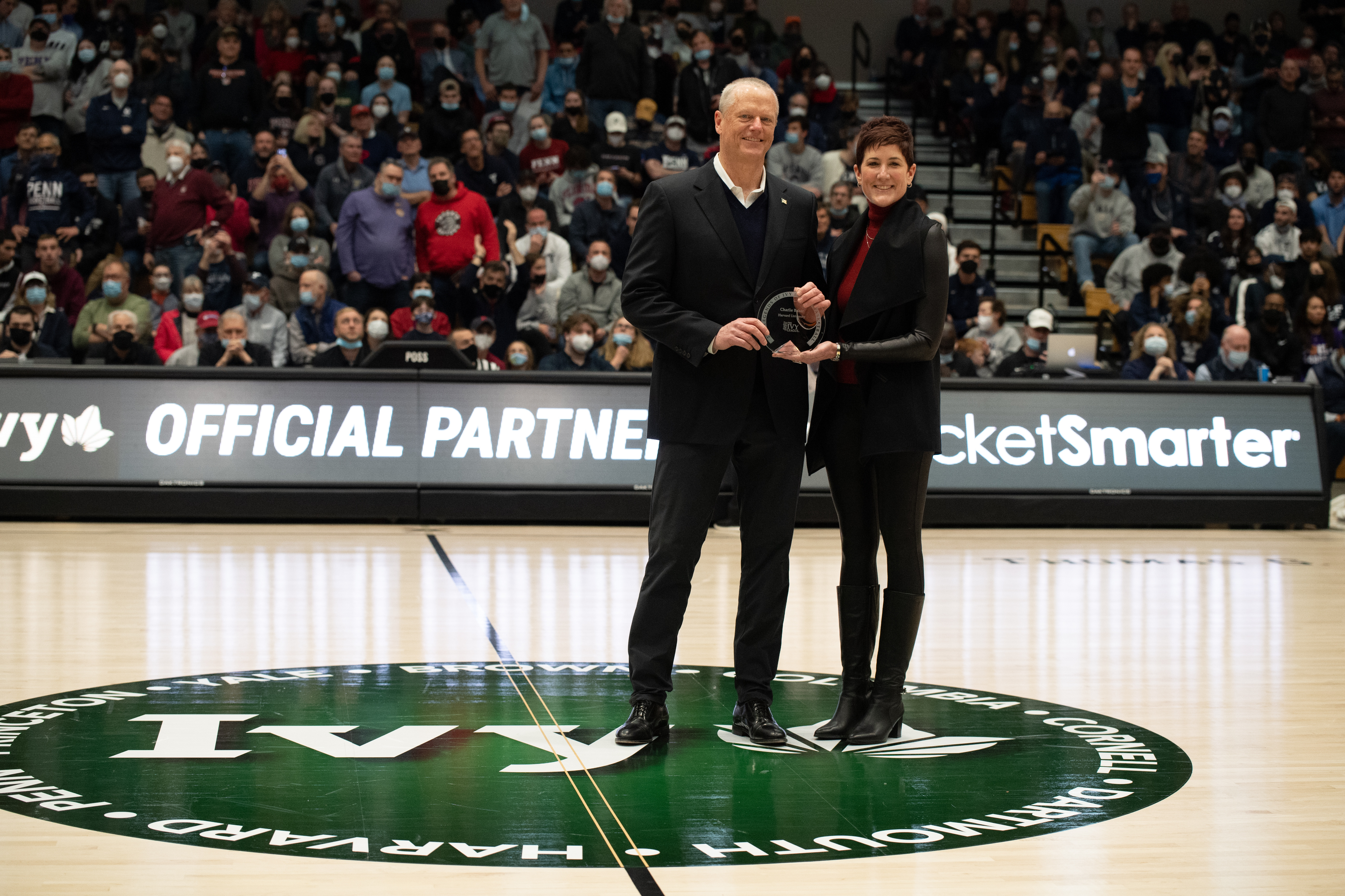 This March 12, 2022, file photo shows Massachusetts Gov. Charlie Baker being presented with an award by Harvard University Director of Athletics Erin McDermott to honor him for the Class of 2022 Legends of Ivy League Basketball during the Ivy League Tournament semifinal between the Pennsylvania Quakers and Yale Bulldogs at Lavietes Pavilion in Boston's Allston neighborhood.