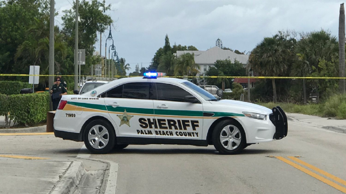  A police car is parked at a crime scene with yellow police tape in the foreground and a road closure sign in the background.