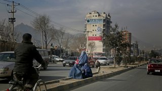 Afghan women sit on a road divider as they seek alms from pedestrians outside a camp for internally displaced people in Kabul, Afghanistan, Dec. 9, 2019.