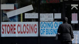 In this May 13, 2020, file photo, a woman looks at signs at a store closed due to COVID-19 in Niles, Ill.,