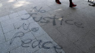A man walks past "No Justice No Peace" spray painted on a sidewalk in downtown Louisville, Ky., June 2, 2020.