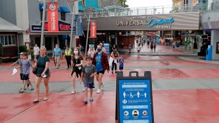 Signs about social distancing and other protocols are seen about the theme park as guests walk by at Universal Orlando Resort