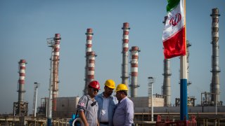 Employees stand near an Iranian national flag at the new Phase 3 facility at the Persian Gulf Star Co. (PGSPC) gas condensate refinery in Bandar Abbas, Iran