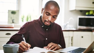 Shot of a man going over paperwork and using his laptop while working from home during the day