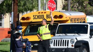 In this file photo a woman wears a facemask picking up a child as an Alhambra Unified School District as a crossing guard stops traffic outside Ramona Elementary School on February 4, 2020 in Alhambra, California.