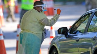 A Healthcare worker help to check in with the assistant from the Florida Army National Guard as vehicles line up at the COVID-19 drive-thru testing center at Marlins Park as the coronavirus pandemic continues on Wednesday, March 25, 2020 in Miami. (David Santiago/Miami Herald/Tribune News Service via Getty Images)