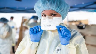 In this April 8, 2020, file photo, medical workers write their names on face masks to identify each other while wearing PPEs at the emergency field hospital run by Samaritan's Purse and Mount Sinai Health System in Central Park in New York City.
