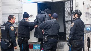 masked officers of the Chelsea Police Department in Chelsea, Massachusetts help a suspect into the back of a police truck