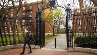 A pedestrian wearing a protective mask exits Harvard Yard on the closed Harvard University campus in Cambridge, Massachusetts, U.S., on Monday, April 20, 2020. College financial aid offices are bracing for a spike in appeals from students finding that the aid packages they were offered for next year are no longer enough after the coronavirus pandemic cost their parents jobs or income.