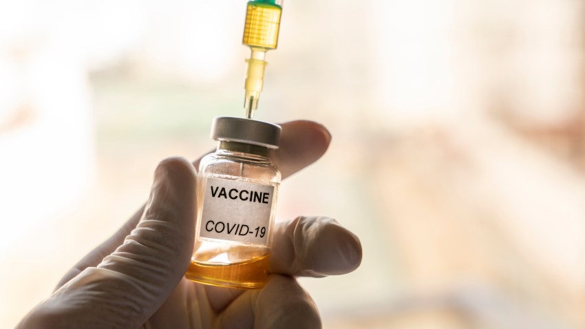 Cropped hand wearing a nitrile glove holding a COVID-19 vaccine vial and a syringe.