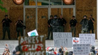 Heavily-armed riot police stand on the porch of the damaged Portland Justice Center during the protests over the death of George Floyd