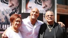 In this May 19, 2015, photo, actor Dwayne "The Rock" Johnson, center, poses with his mom and father Rocky Johnson at a ceremony honoring the actor at TCL Chinese Theatre IMAX in Hollywood, California. WWE said in a statement that Rocky Johnson, a WWE Hall of Famer, died at 75 on Wednesday.