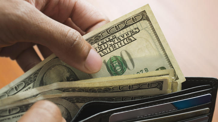 A hand pulls bills out of a wallet.
