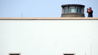 A man uses binoculars atop the United States embassy in Tunis, Wednesday, Sept. 12, 2012 as Muslims demonstrate outside the embassy to demand the closure of the embassy and the departure of the ambassador.