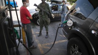 A soldier stand guard as a customer wearing a protective face mask fills up his gas tank, amid a nationwide quarantine to slow the spread of the new coronavirus, in Caracas, Venezuela, Tuesday, April 7, 2020.