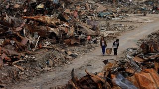 In this Thursday, April 7, 2011, file photo, two women walk past debris in an area devastated by the March 11 earthquake and tsunami in Ishinomaki, Miyagi Prefecture, northern Japan.