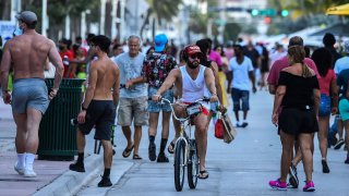 A man rides a bicycle as people walk on Ocean Drive in Miami Beach, Florida on June 26, 2020.