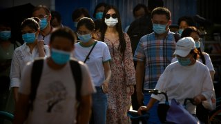 People wearing face masks to protect against the coronavirus wait to cross an intersection in the central business district in Beijing
