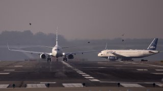 An American Airlines plane departs next to a JetBlue Airways plane taxiing at Reagan National Airport in Arlington, Va., April 6, 2020.