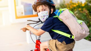 Little boy riding a bicycle wearing a protective mask.