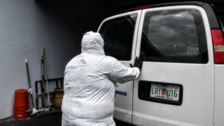 Funeral assistant, Bradley Georges 26 pull out a stretcher from a van wearing a PPE kit prior to a funeral at one of Miami's largest funeral homes, Van Orsdel funeral homes in Miami, on July 17, 2020. - For one young funeral assistant in Florida, his social life has been dead -- his only human interactions are coronavirus victims at the funeral home where he works. But he doesn't regret his isolation. The pandemic is "bigger than we are," said Bradley Georges, 26, an assistant at the Van Orsdel funeral home in Miami.