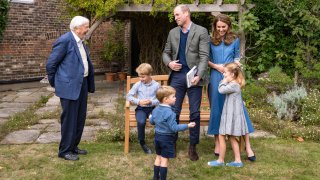 Britain's Prince William, centre, and Kate, the Duchess of Cambridge, react with Naturalist David Attenborough, left, with their children, Prince George, seated, Princess Charlotte, right and Prince Louis, foreground, in the gardens of Kensington Palace