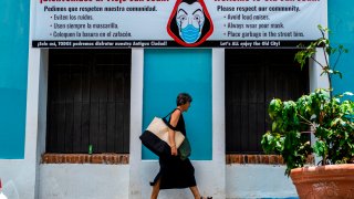 A woman walks pass by a banner urging visitors to wear face masks in San Juan, Puerto Rico