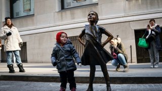 A child stands next to the ‘Fearless Girl’ after a ceremony to unveil the statue’s new location across from the New York Stock Exchange on Dec. 10, 2018 in New York City.