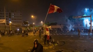 A protester holds a banner with the country's national color as police launch tear gas to disperse protesters who gathered at Plaza San Martin as part of a protest against newly appointed interim president Manuel Merino on November 14, 2020 in Lima, Peru.