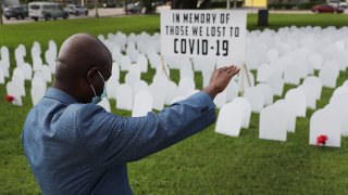 Vice Mayor Alix Desulme, City of North Miami, raises his arm during a prayer for local lives lost to COVID-19 as a memorial to those lost is unveiled at Griffing Park on October 28, 2020 in North Miami, Florida. Five hundred plastic cardboard tombstones were placed in the ground honoring COVID-19 victims.