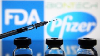 In this photo illustration, vials and a medical syringe seen in front of the Food and Drug Administration (FDA) of the United States and Pfizer Pharmaceutical company logos. FDA approves Pfizer/BioNTech the COVID-19 coronavirus vaccine for emergency use in the US, reportedly by media.