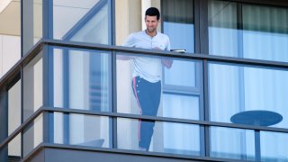 Serbia's Novak Djokovic stands on the balcony at his accommodation in Adelaide, Australia, Tuesday, Jan. 19, 2021. Australian Open tournament director Craig Tiley defended Djokovic for appealing to Australian Open organizers to ease restrictions so players could move to private residences with tennis courts.