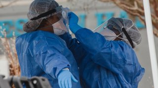 Healthcare workers from the Medical University of South Carolina clean each other's gear at a COVID-19 testing site in a parking lot