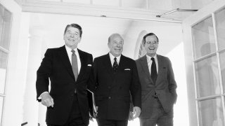 Secretary of State George Shultz, center, walks with President Ronald Reagan and Vice President George Bush