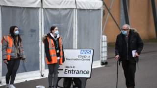 A man walks past volunteers at a temporary vaccination hub set up to administer a Covid-19 vaccine, at the Colchester Community Stadium in Colchester, Essex, south east England on February 6, 2021.