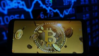 In this photo illustration a Bitcoin logo seen displayed on a smartphone with stock market percentages in the background.