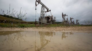 Oil pumping jacks, also known as “nodding donkeys”, are reflected in a puddle as they operate in an oilfield near Almetyevsk, Russia, on Sunday, Aug. 16, 2020.