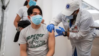 Dr. Jerry Abraham, director of Kedren Vaccines, right, gives a COVID-19 vaccination to Jose Guzman-Wug, 16, while his mom, Adriana Wug, watches at Kedren Health on Thursday, April 15, 2021 in Los Angeles, CA.