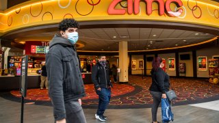 People wear face masks as they walk by a movie theater during the coronavirus disease (COVID-19) pandemic in Newport, New Jersey, April 2, 2021.