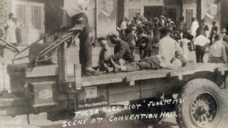 This photo provided by the Department of Special Collections, McFarlin Library, The University of Tulsa shows a truck parked in front of the Convention Hall with a Black man whose condition is unknown lying on the bed of a truck during the Tulsa Race Massacre in Tulsa, Okla