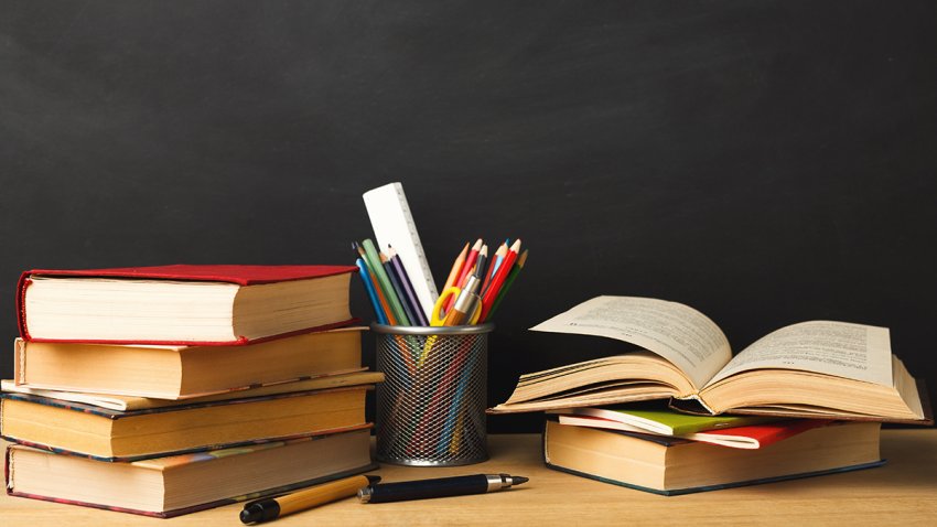 Educational background. Books piles and pencils against empty classroom blackboard for copy space.