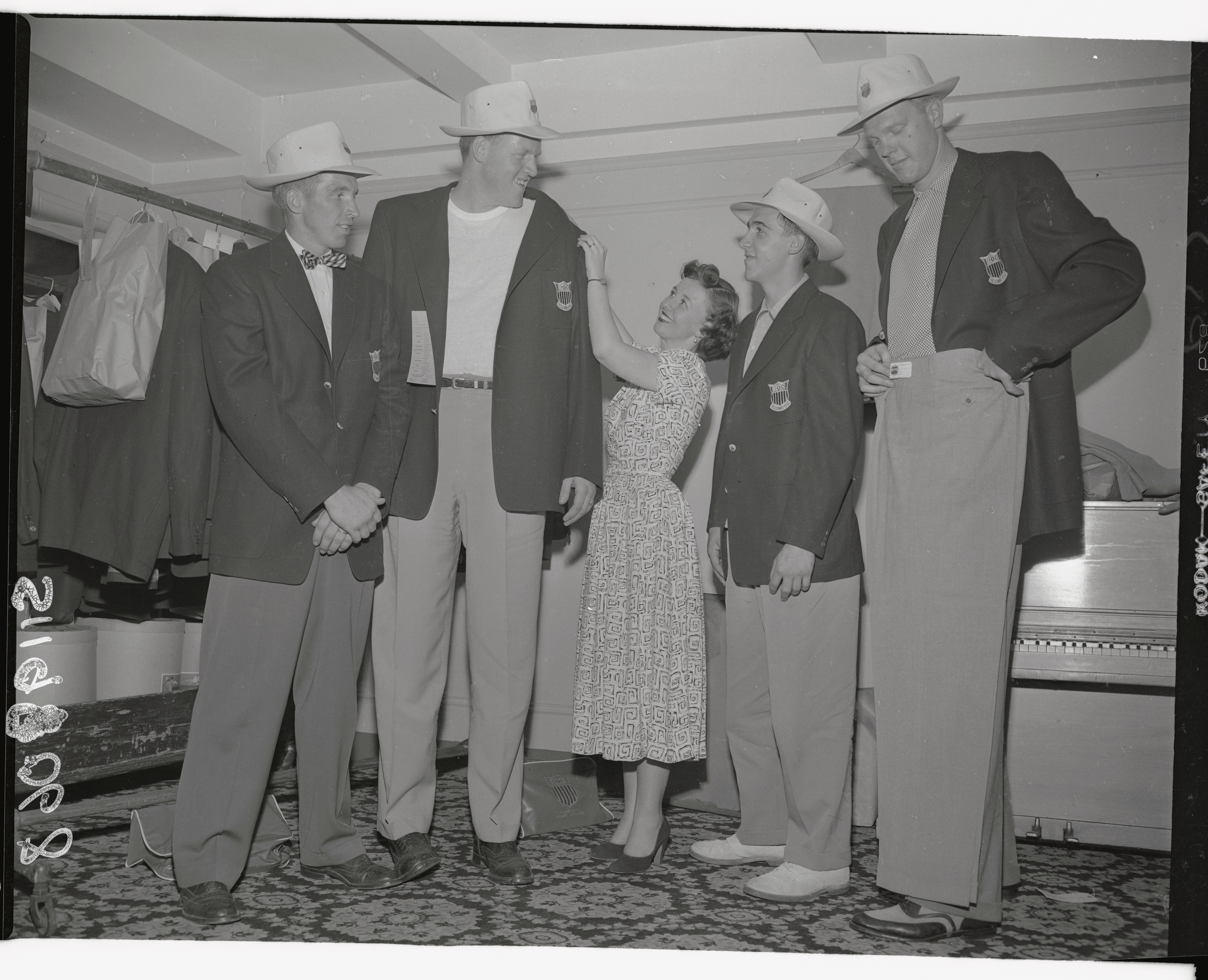 Eleanor McCoy is dwarfed by athletes (from left) Howard William, Clyde Lovelette, both of Peoria, Illinois; Clyde Dean Kelly of Lawrence, Kansas, and Bob Kurland of Bartsville, Oklahoma, as she checks to make certain their Olympic jackets fit in 1952.