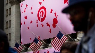 Pedestrians pass in front of Pinterest signage displayed outside of the New York Stock Exchange.