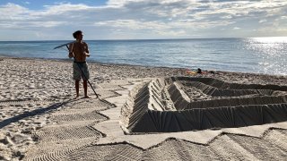 Sand sculptors adorns the beach beside the area that is closed for search and rescue operations at the partially collapsed Champlain Towers South condo building
