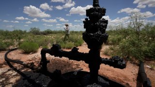 Ashley Williams Watt walks near a wellhead and flowline at her ranch, Friday, July 9, 2021, near Crane, Texas. The wells on Watt's property seem to be unplugging themselves. Some are leaking dangerous chemicals into the ground, which are seeping into her cattle's drinking water. And she doesn't know how long it's been going on.