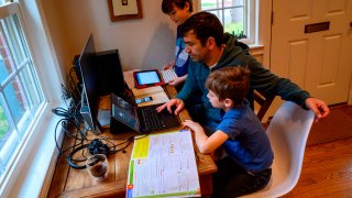 Joachim (R), 8, and Colin (L), 10, whose school was closed following the Coronavirus outbreak, do school exercises at home with their dad