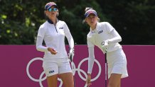 Jessica Korda and Nelly Korda stand in front a pink fence with the Olympic Rings.