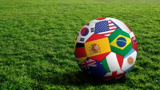 A soccer ball with flags of the world on it sitting on grass