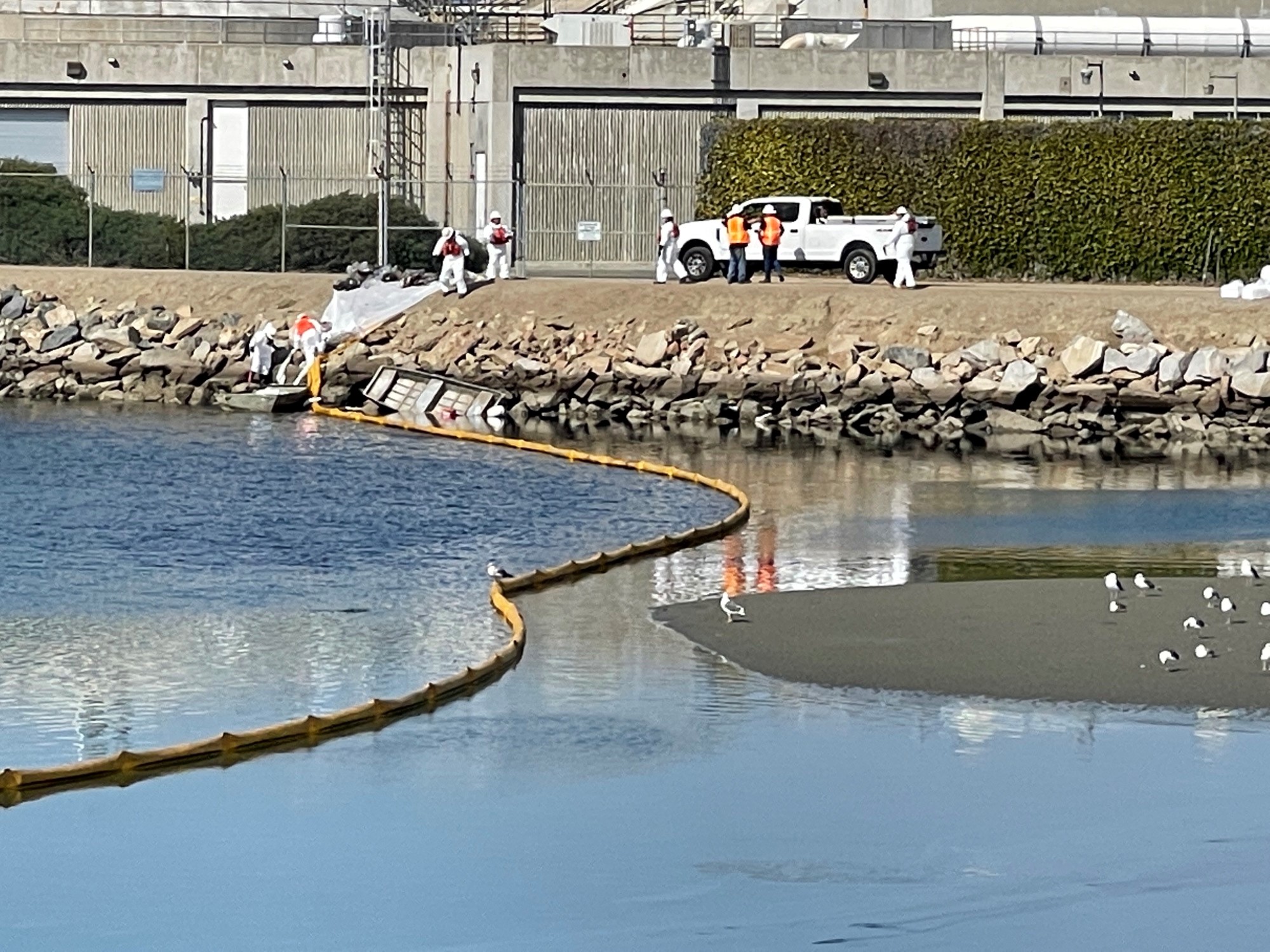 The spill drew a response from all levels of government, and a unified command led by the United States Coast Guard was established to handle the environmental crisis. In this photo, cleanup workers at the Huntington Beach Channel work to clean up the spill.