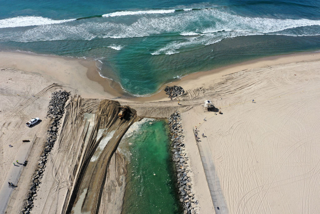 HUNTINGTON BEACH, CALIFORNIA &#8211; OCTOBER 04: In an aerial view, a crew works to block oil in the ocean (TOP) from entering an inlet (BOTTOM) leading to the Talbert Marsh wetlands after a 126,000-gallon oil spill from an offshore oil platform on October 4, 2021 in Huntington Beach, California. The spill forced the closure of the popular Great Pacific Airshow yesterday with authorities closing beaches in the vicinity.  (Photo by Mario Tama/Getty Images)